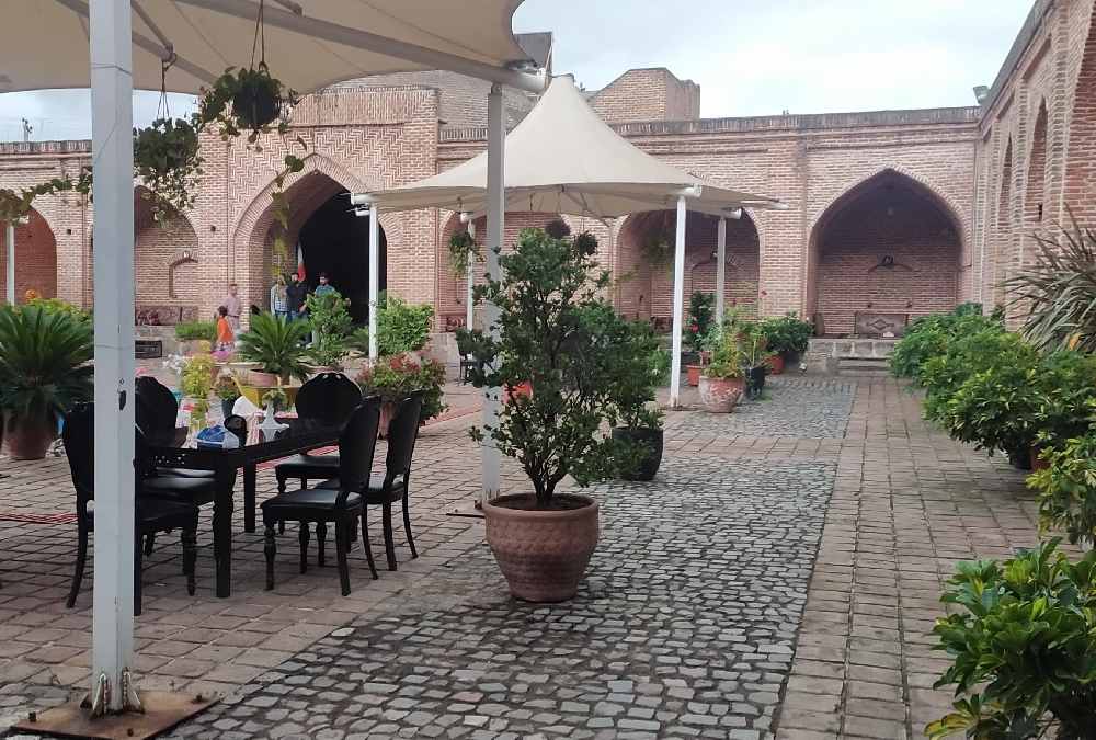 حیاط داخلی کاروانسرای شاه عباسی رشت مزین به گل و گیاه و آلاچیقهای سفید چادری و میز و صندلی