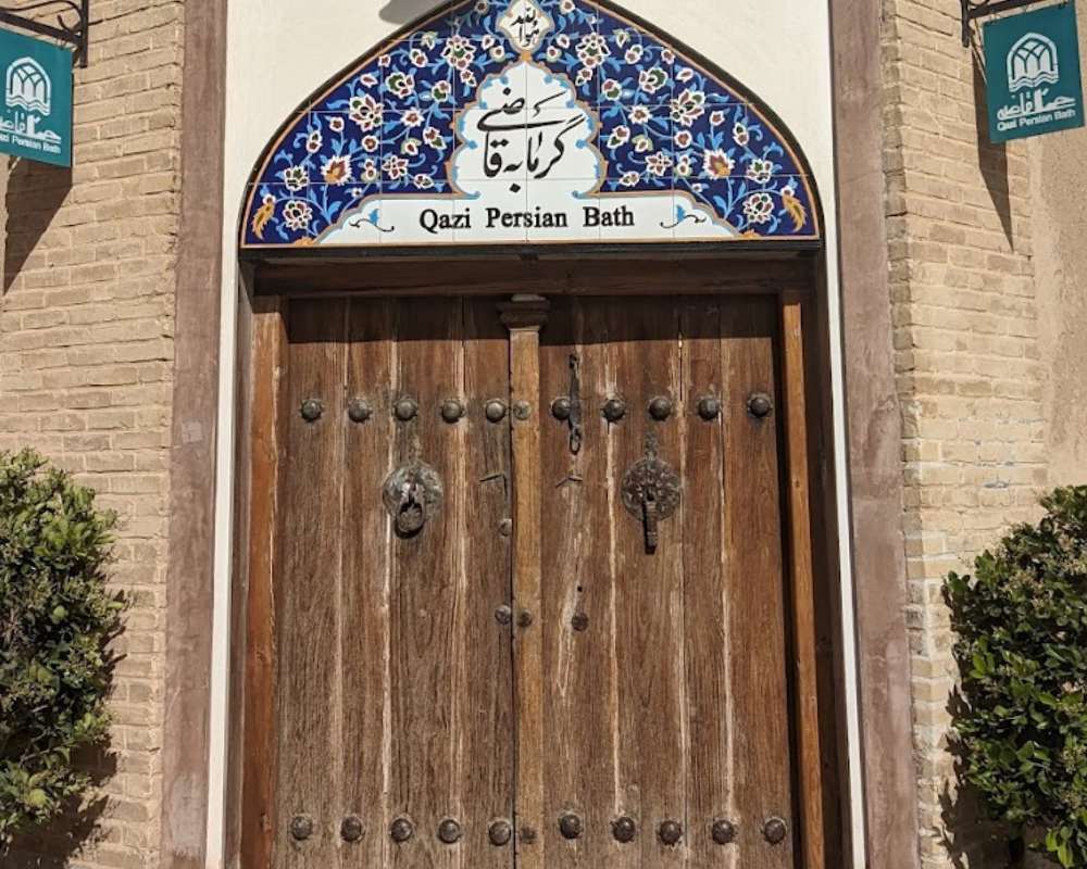 نمایی از درب ورودی گرمابه قاضی با دیوارهای آجری و درب چوبی