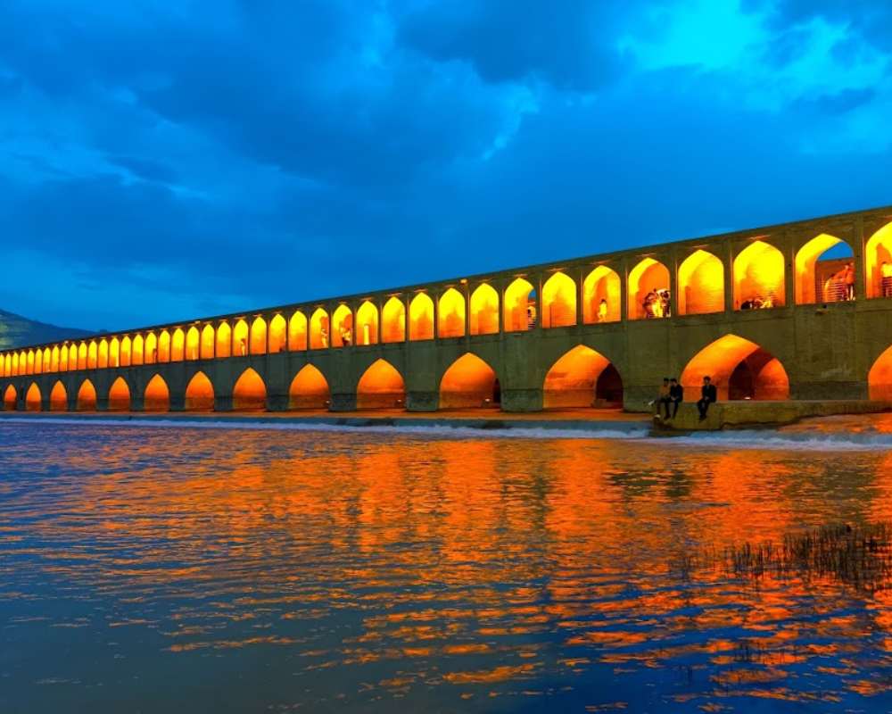 نمایی از غروب سی و سه پل با نور زرد رنگ داخل بنا و آسمان ابری