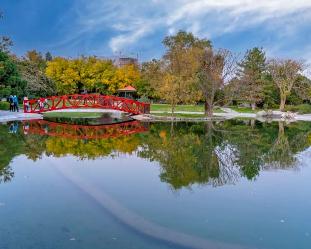 انعکاس پل قرمز و درختان سبز و زرد در دریاجه باغ گیاه شناسی تهران