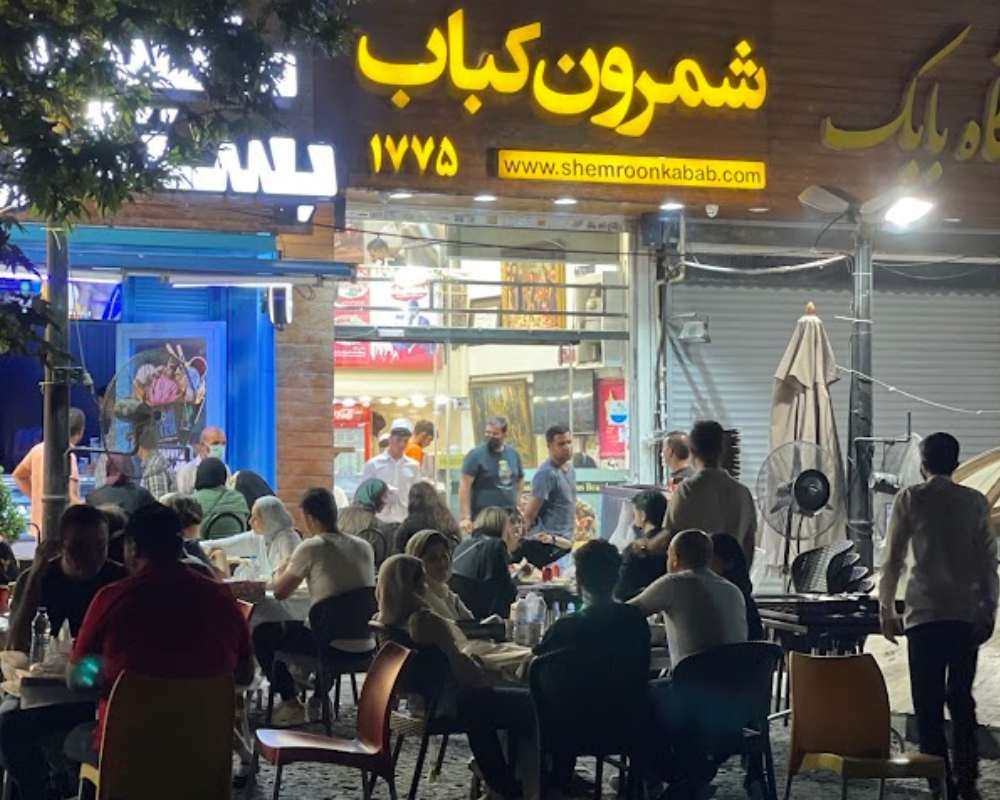 محوطه بیرونی رستوران شمرون کباب در شب که توسط مشتریان شلوغ شده است