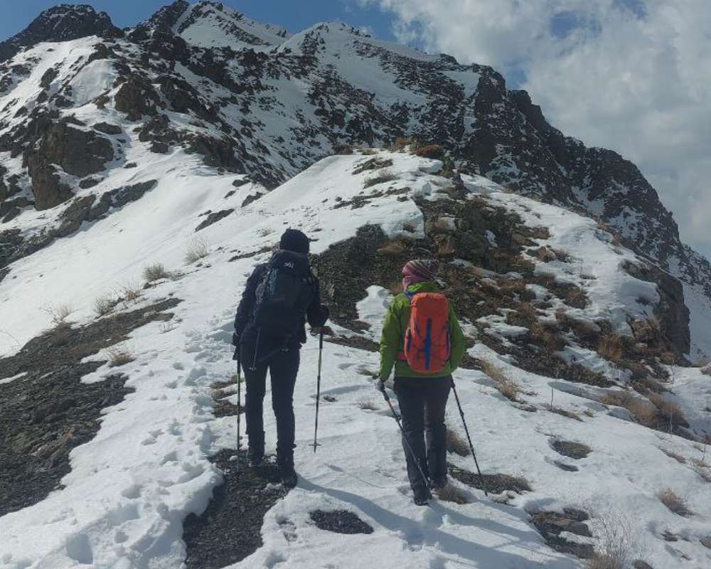 خانم و آقایی در حال کوهنوردی در کوه‌های برفی روستای سنگان