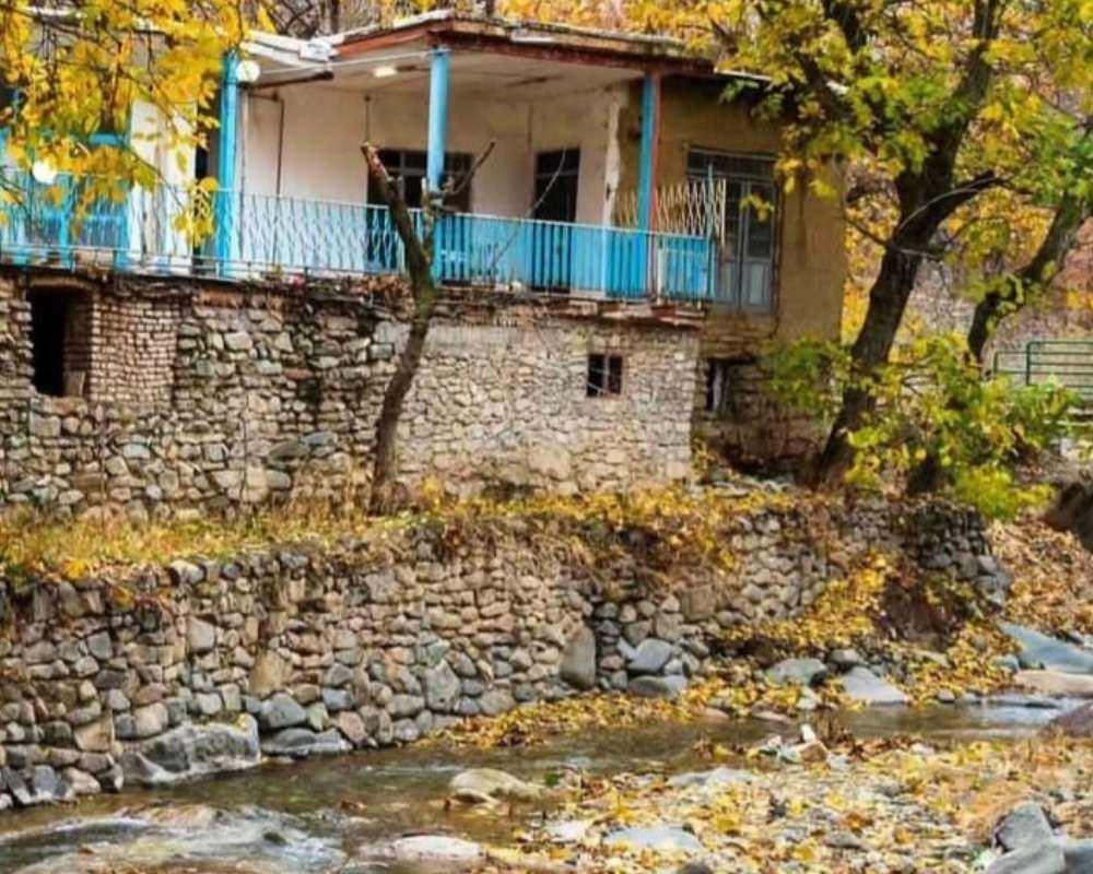 نمایی از خانه ای با نرده های آبی و رودخانه در فضای پاییزی روستای سنگان