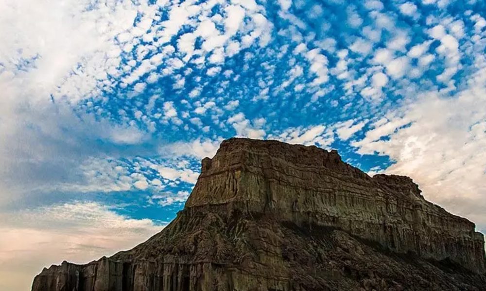 صخره بزرگ زیر آسمان آبی با ابرهای پنبه ای پراکنده قشم