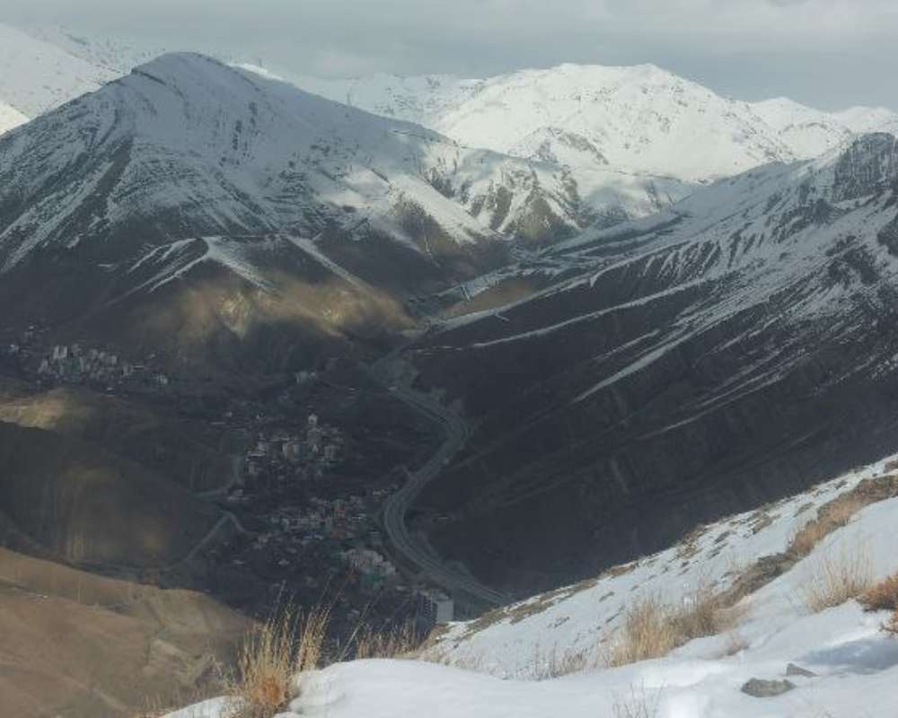 نمایی از روستای سنگان از میان کوه‌های برفی زمستان