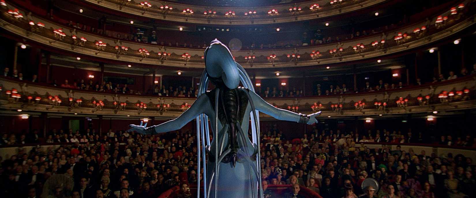 خواننده اپرای بیگانه با پوست آبی، از پشت دیده می‌شود که در حال خواندن برای یک سالن اپرای پرجمعیت در فیلم عنصر پنجم است