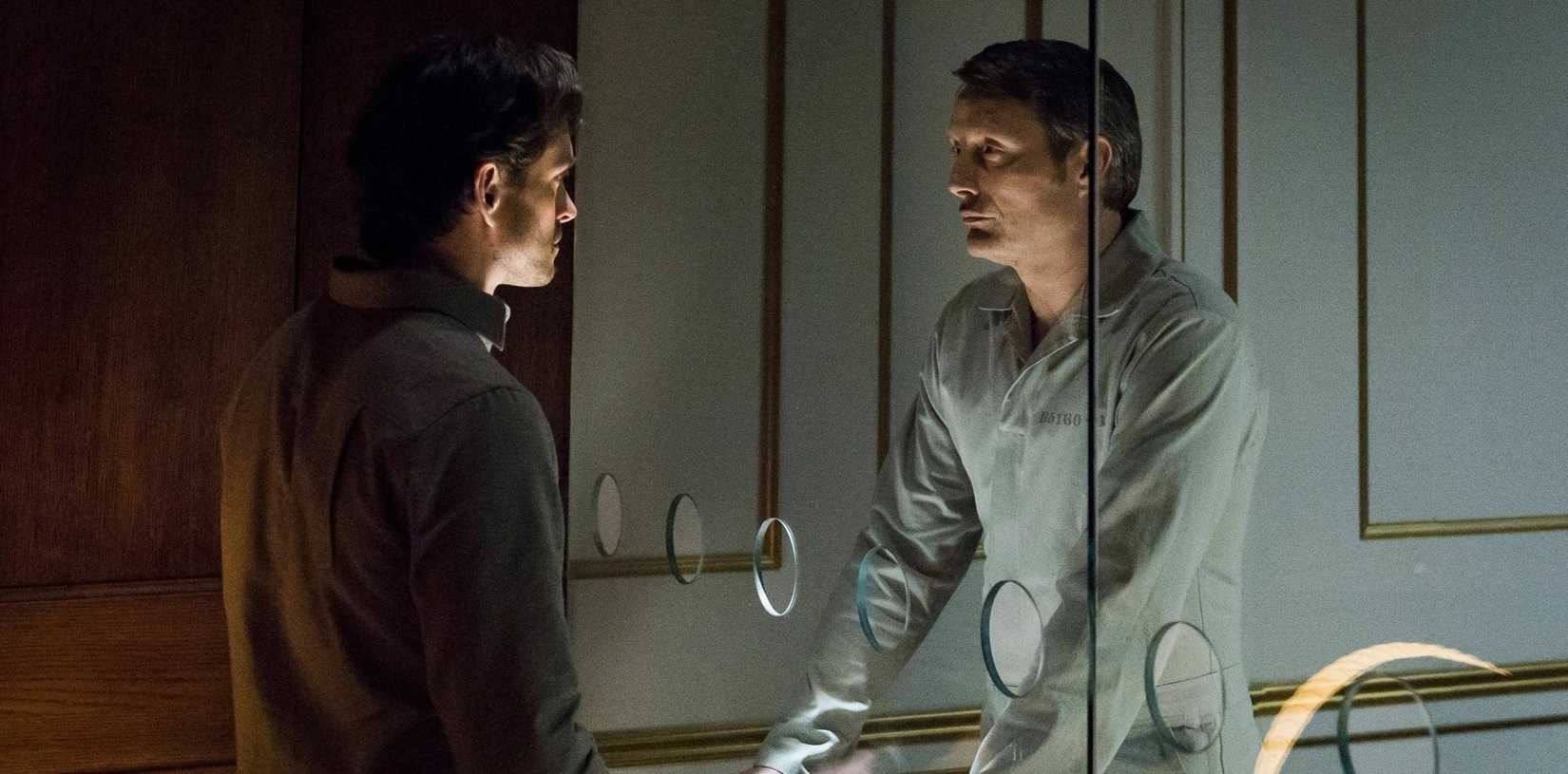 هانیبال لکتر (مدس میکلسن)، در یک لباس پلاستیکی کامل بر روی یک کت و شلوار سه تکه، پشت یک میز ایستاده و سر قربانی نشسته‌ای را که سرش به عقب پرتاب شده در دست دارد در سریال هانیبال از NBC