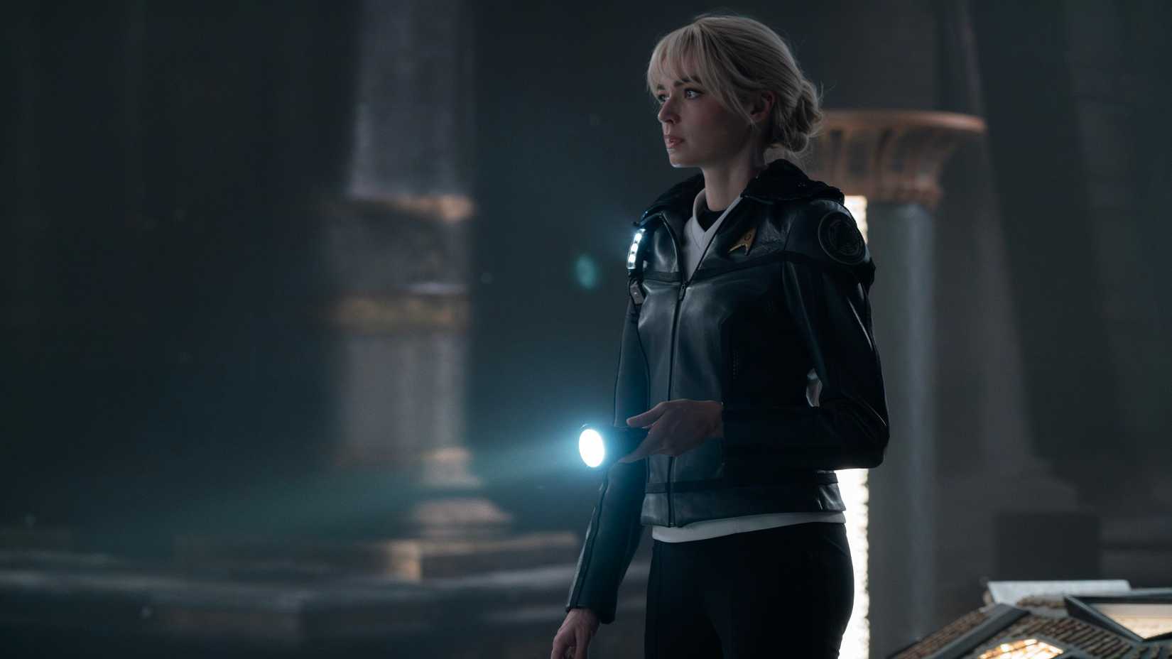 جسی بوش در نقش کریستین چپل در حال نگه داشتن چراغ قوه و کاوش در یک معبد بیگانه در Star Trek: Strange New Worlds